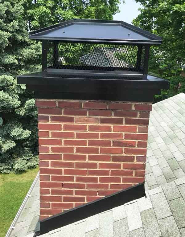 Chimney with custom black chimney cap neat and clean with trees in the background.