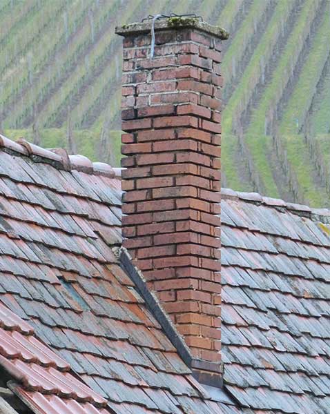 Leaky Chimneys - tall chimney with spalling with fields in the background.