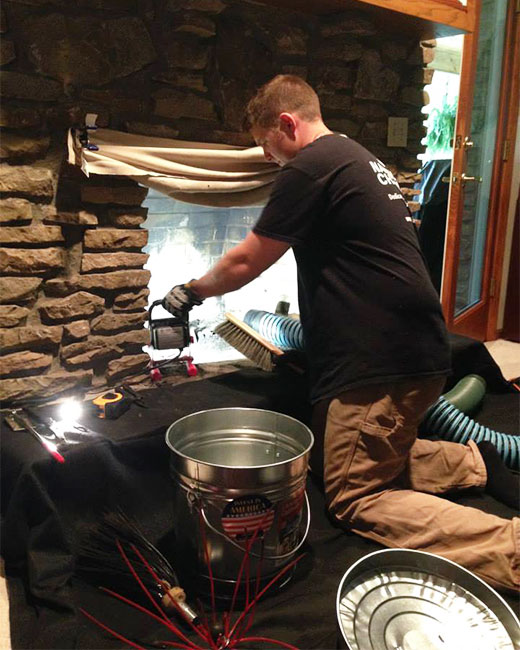 Tech cleaning stack rock fireplace with broom and vacuum and bucket in front.