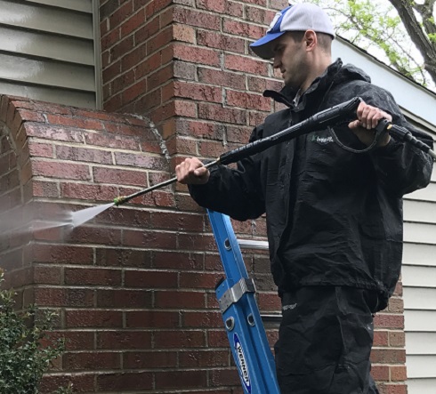 ChimneySaver Water Repellent tech standing on ladder power washing brick.